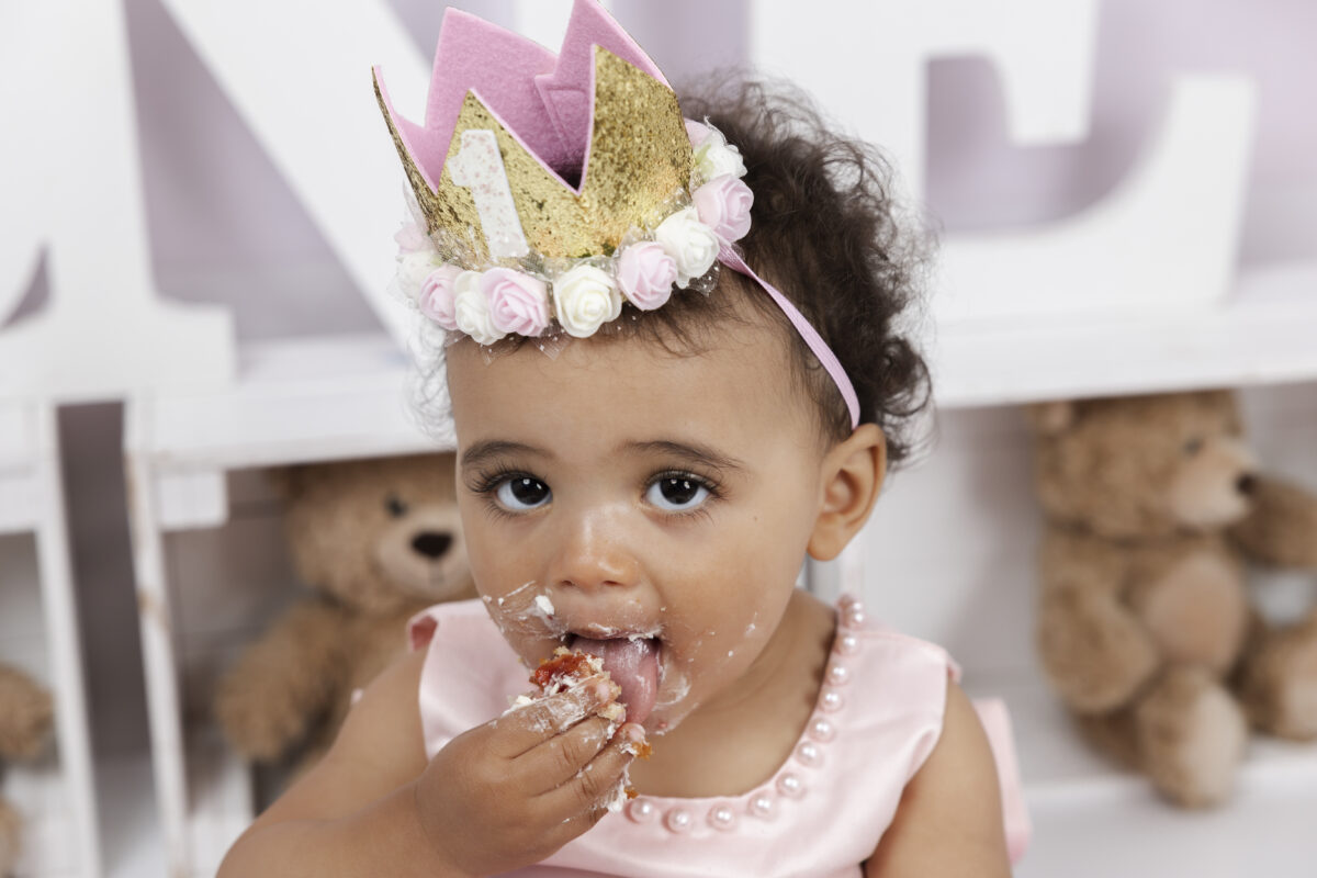 Baby girl in pink crown eating cake during first birthday
