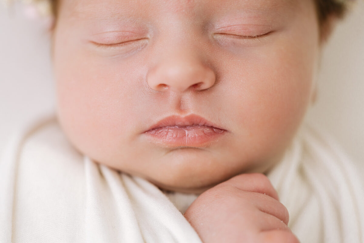 Close-up of a sleeping newborn baby's face, focusing on closed eyes, nose, and lips, wrapped in soft fabric.