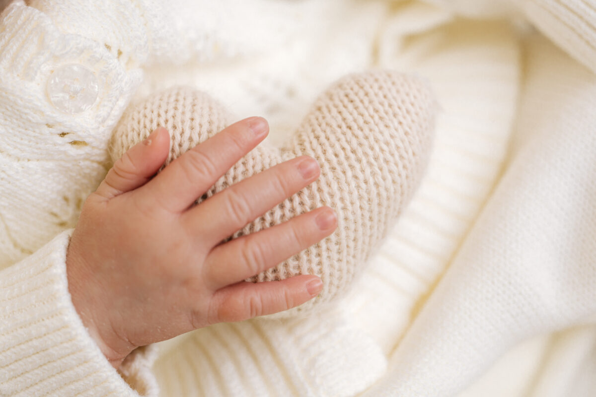 Newborn baby's hand gently resting on a knitted heart prop during a photography session at Little Miracles Photography Studio.
