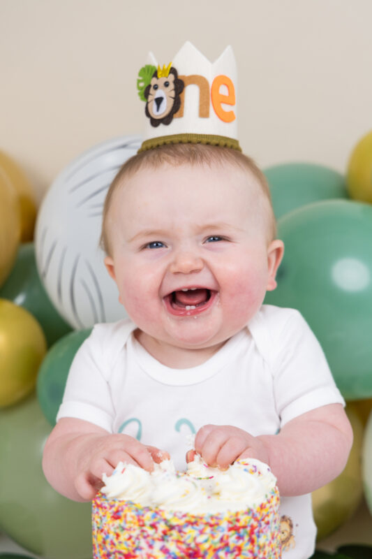 Laughing baby boy with "one" crown doing cake smash