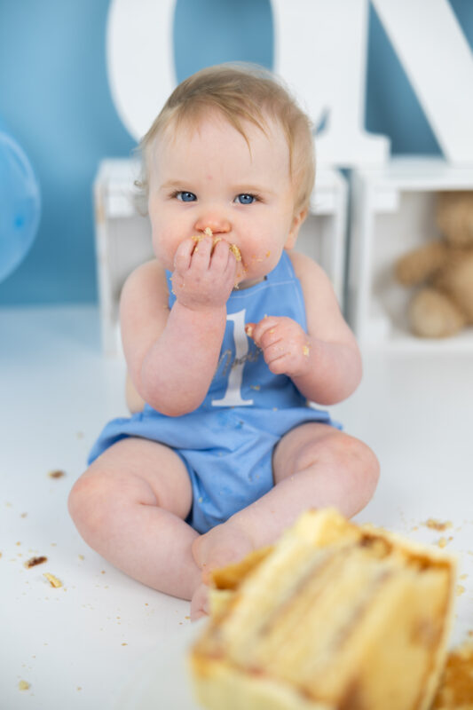 Baby boy eating cake during first birthday cake smash
