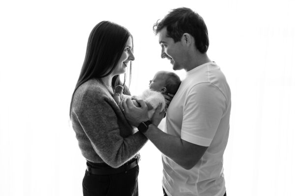 Black and white family portrait of parents with newborn baby.