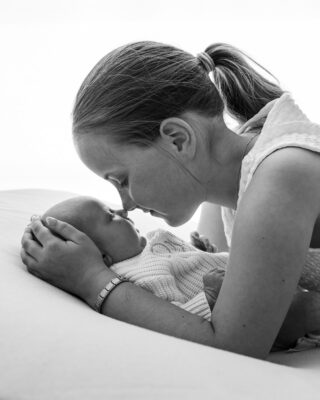 Black and white portrait of sister kissing newborn baby.