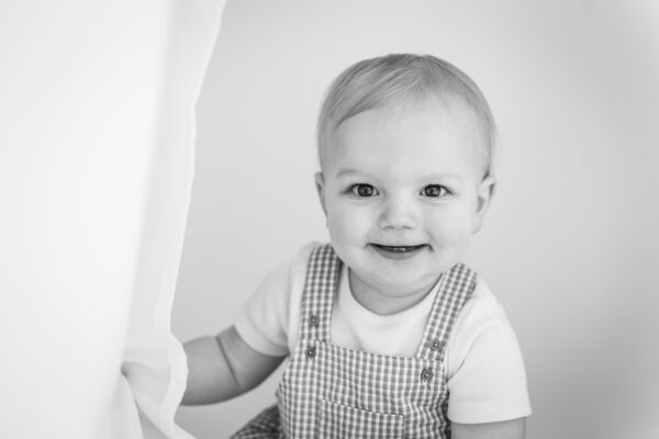 Black and white portrait of baby boy in striped dungarees.