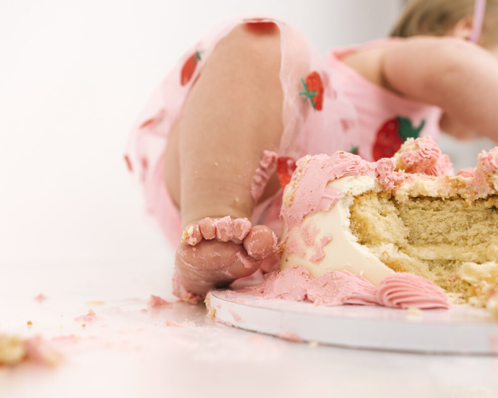 Smiling baby girl celebrating her first birthday with pink and red strawberry bunting.