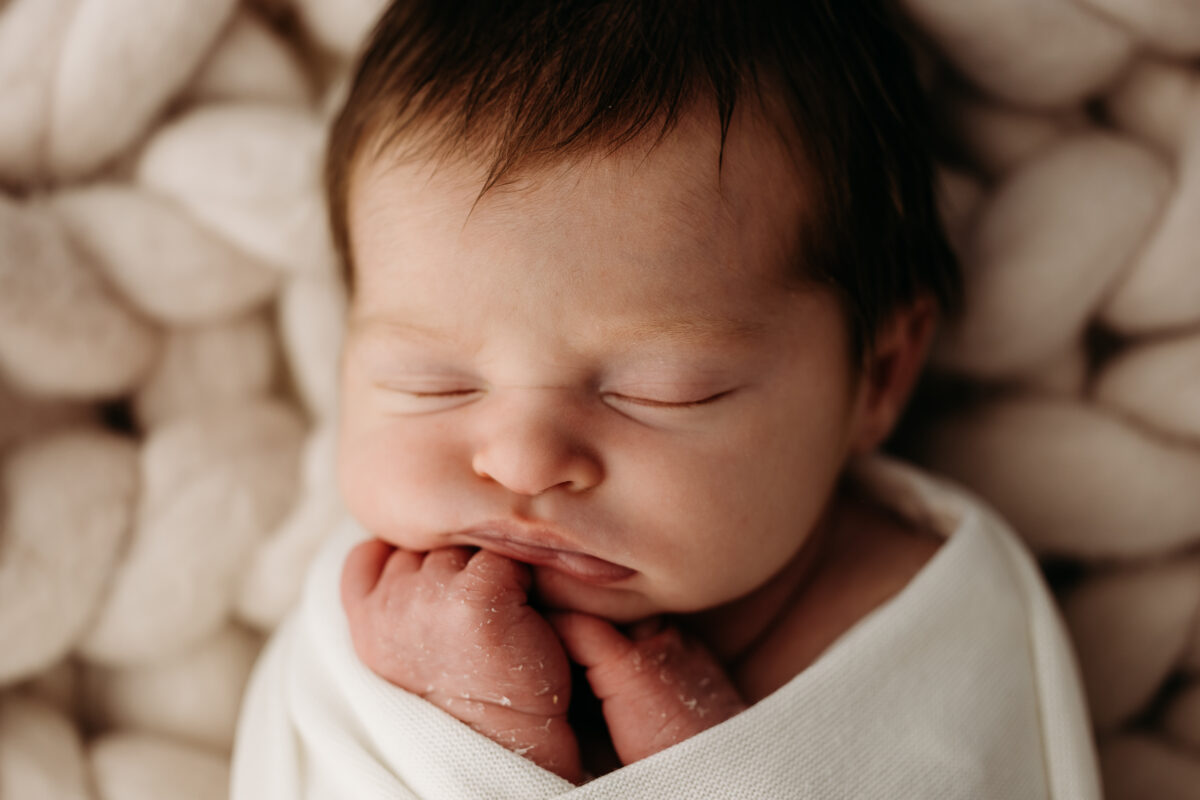 Close-up of sleeping newborn with hands beneath chin.