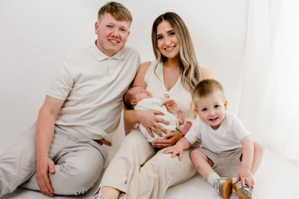 Mum, dad and big brother smiling together while holding their newborn baby.