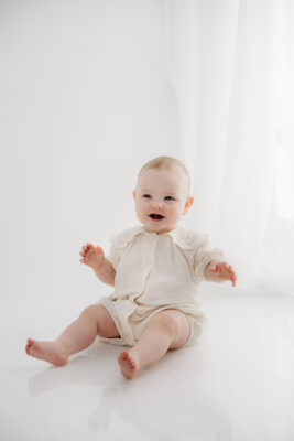 Smiling baby photographed against a neutral studio backdrop.