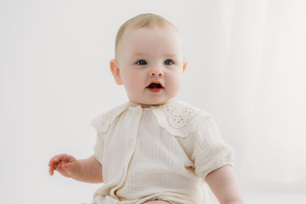 Smiling baby photographed against a neutral studio backdrop.
