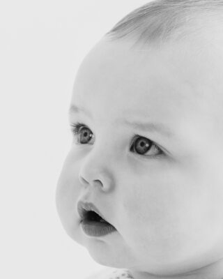 Smiling baby photographed against a neutral studio backdrop.
