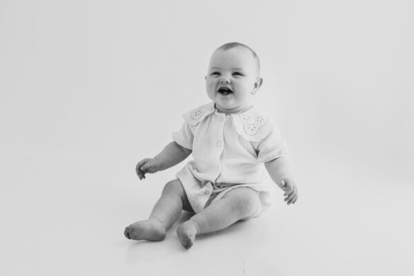 Smiling baby photographed against a neutral studio backdrop.