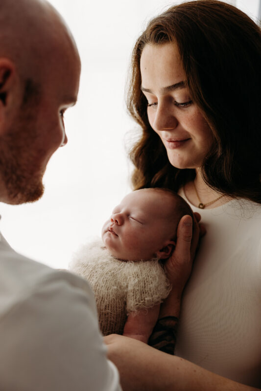 Parents admiring newborn baby in warm natural light.