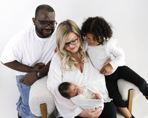 Parents and older sibling cuddling newborn baby in family portrait.