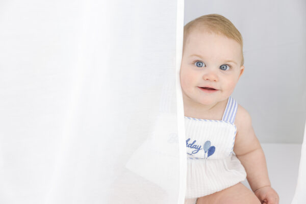 Baby boy peeking through a white curtain.