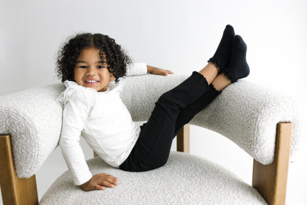 Playful older sibling sitting on a white chair.