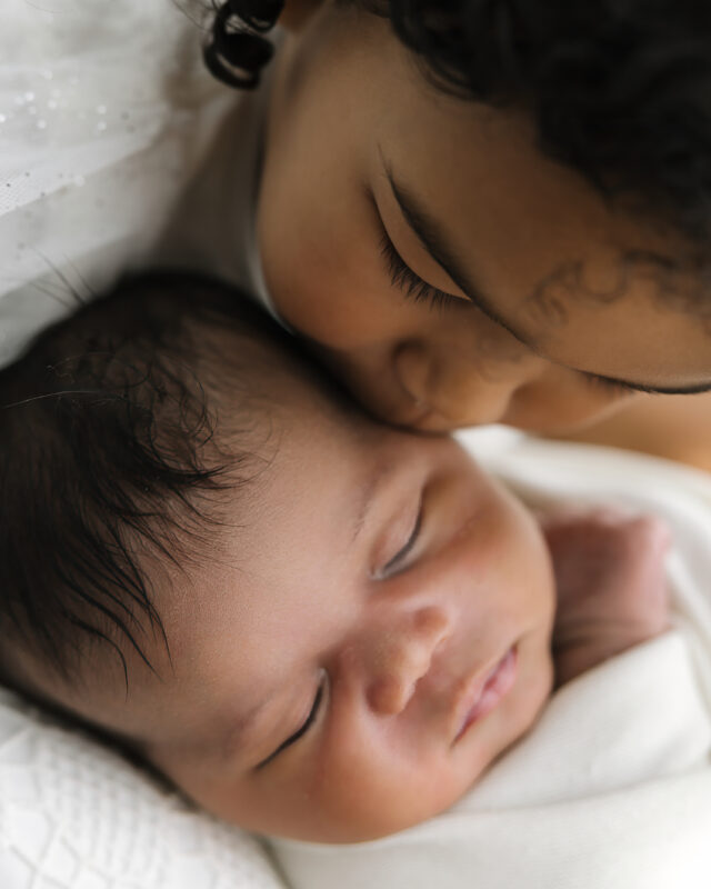 Older sibling kissing sleeping newborn baby.