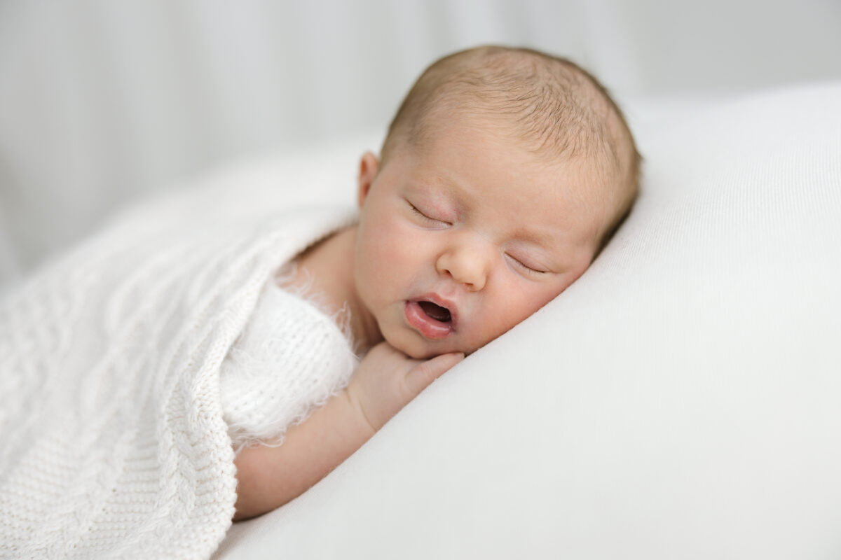 Sleeping newborn resting on white cushion.