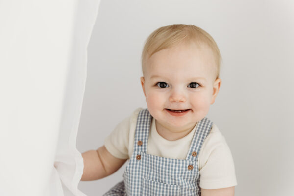 Smiling baby boy in blue striped dungarees.