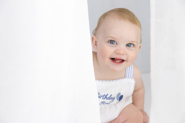 Baby boy smiling behind a white curtain.