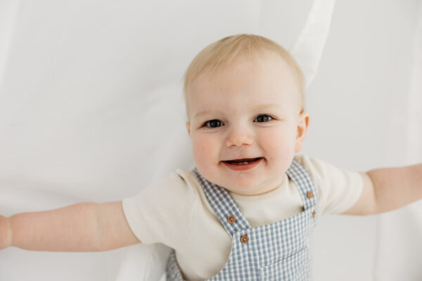 Black and white portrait of baby boy in striped dungarees.