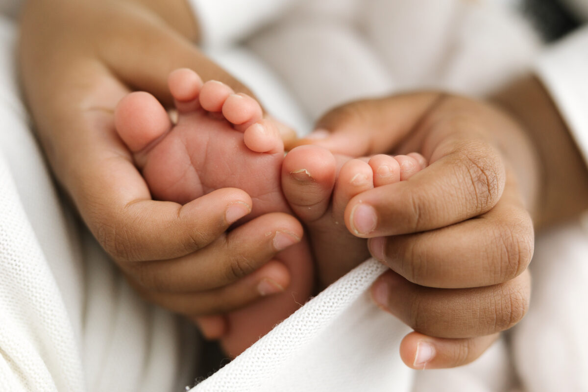 Tiny newborn feet held gently in sisters hands.