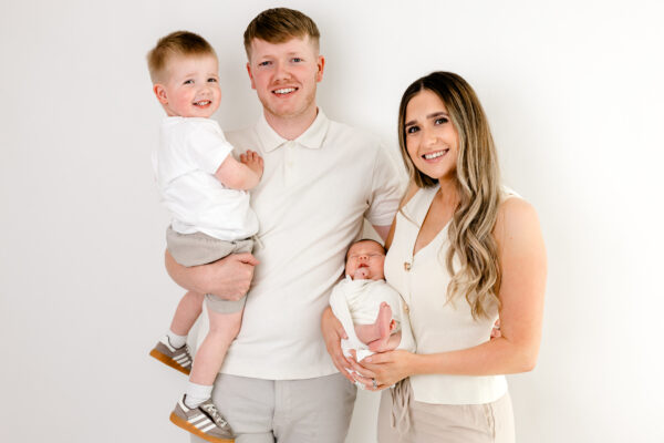 Young boy smiling while playing with a white curtain during a family photography session.