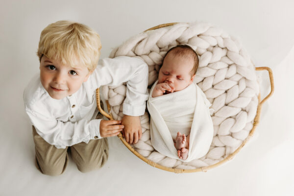 Young sibling beside newborn baby resting in a wicker basket.